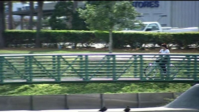 Video frame of a woman riding a bike over a pedestrian bridge